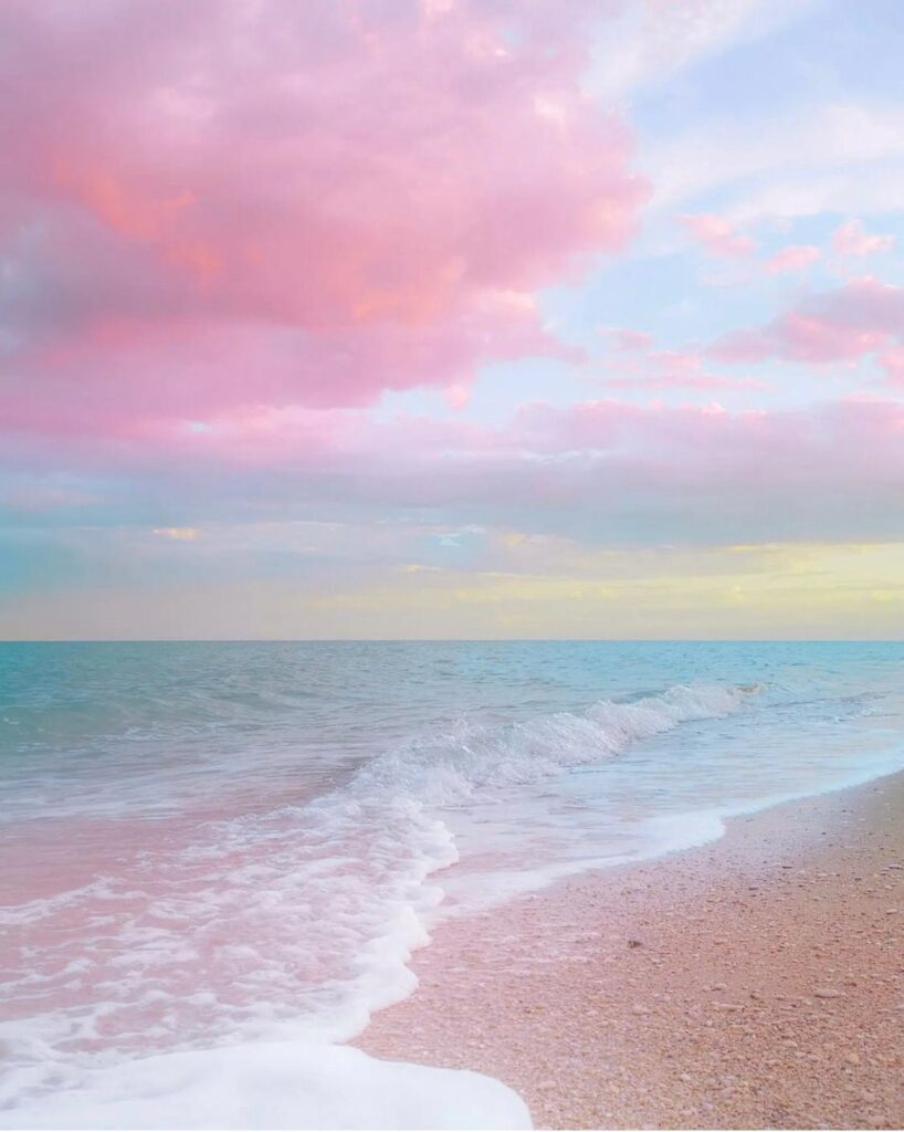 Pastel pink sunset over a calm beach with turquoise water and gentle waves.