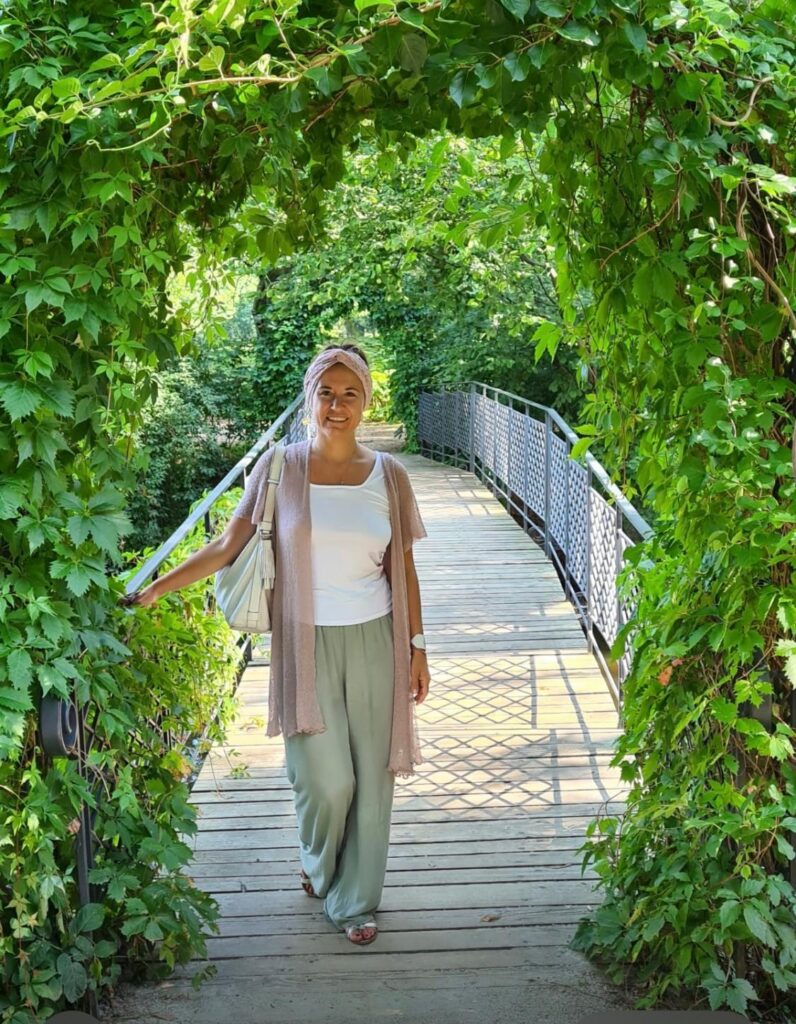 Dr. Kamila Hortyńska smiling on a wooden bridge framed by leafy vines.