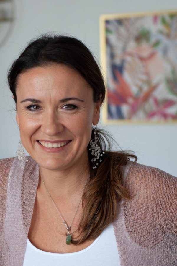 Close-up portrait of a smiling Dr. Kamila Hortyńska, with brpwn hair tied loosely, wearing elegant beaded earrings and a mauve knit top.
