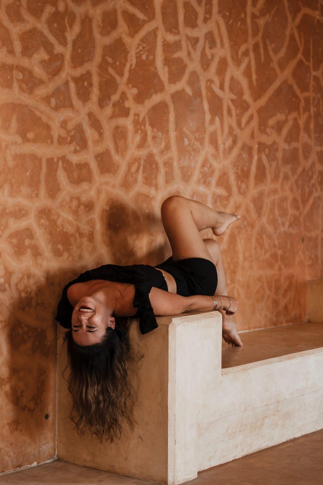 A woman laughing as she reclines on a stone bench
